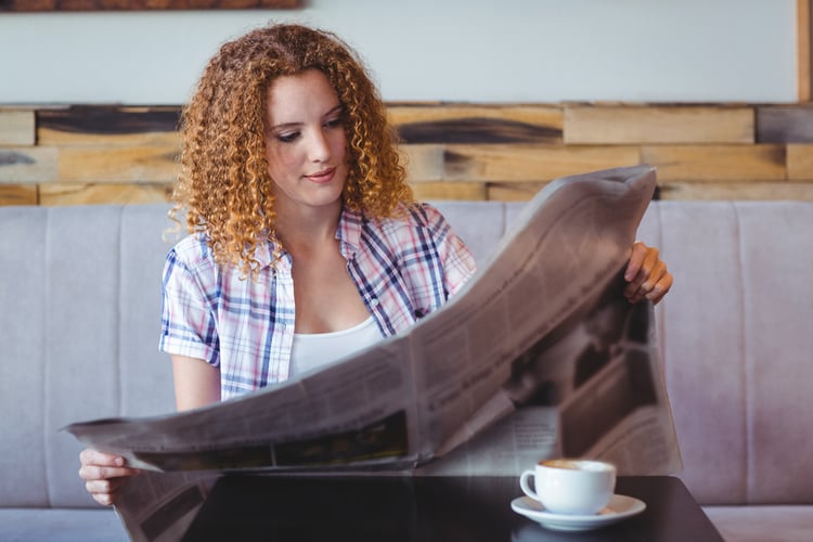 Pretty curly hair girl having cup of coffee and reading newspaper at the cafe