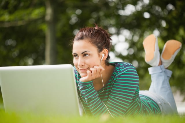 Thoughtful casual student lying on grass using laptop on campus at college