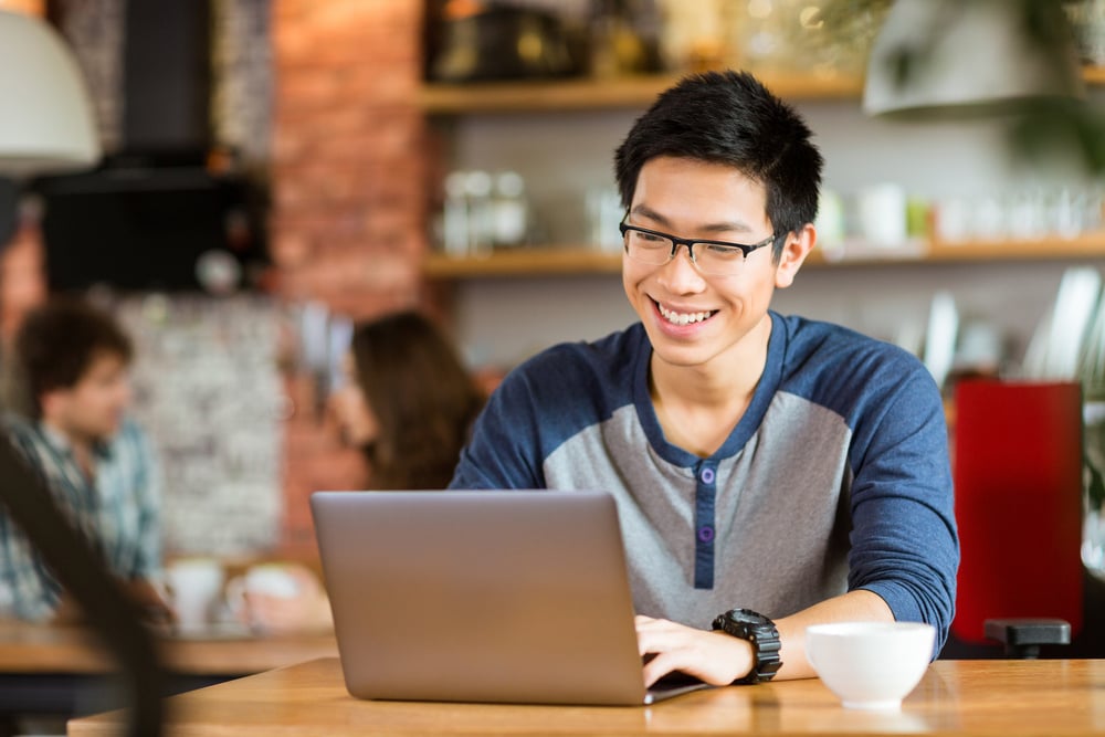 advertise to students with emerging media - college student smiling while using laptop at a coffeeshop