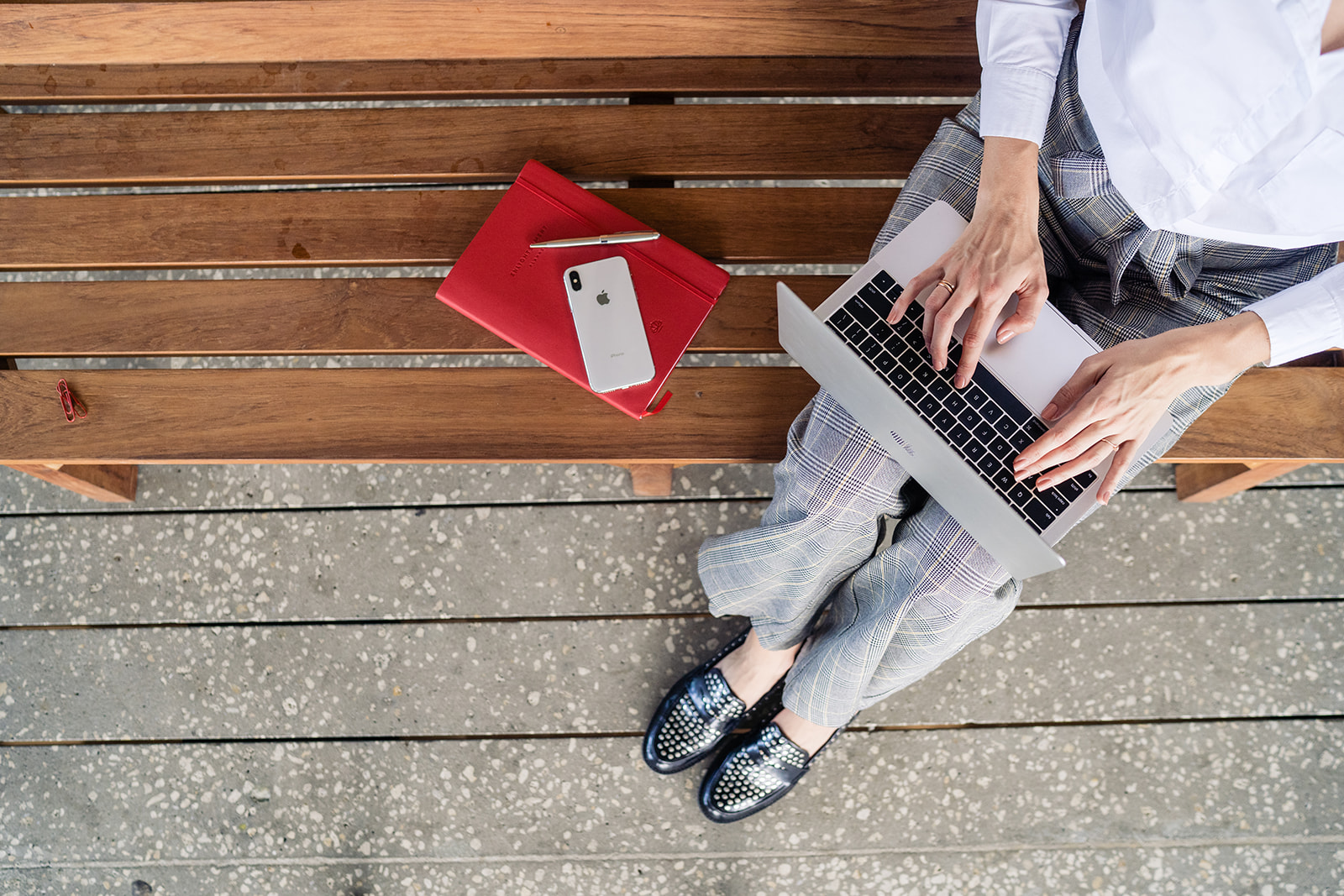 digital marketing agency employee sitting on a bench while using a laptop with a mobile phone and a notebook next to her