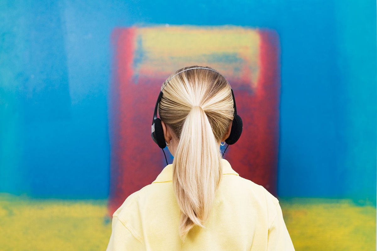 Young blonde woman with headphone in front of a colorful background